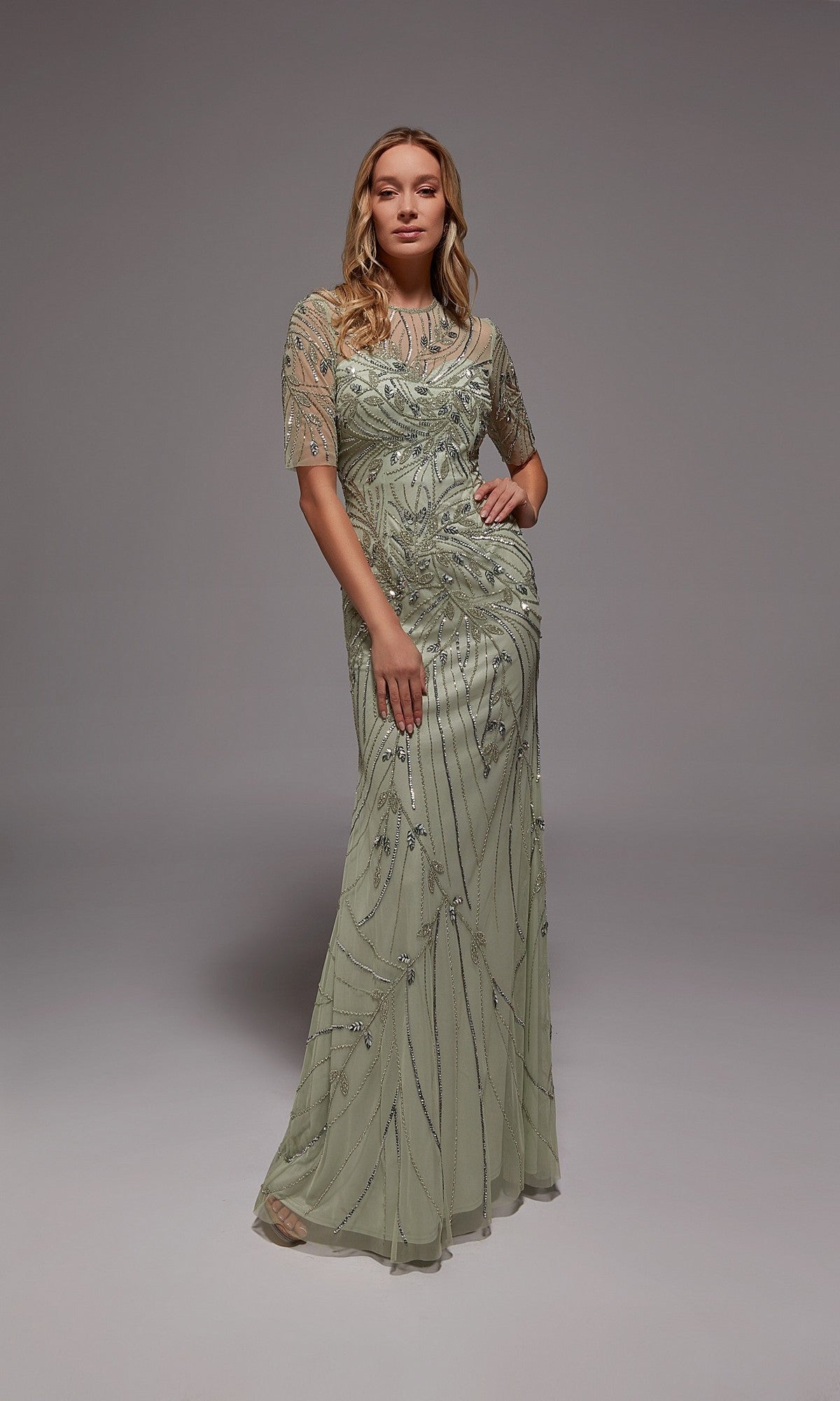 A woman in the Alyce 27809 Long Formal Dress, a floor-length light green gown with short sleeves and intricate beading, ideal for formal occasions, stands against a plain gray background.